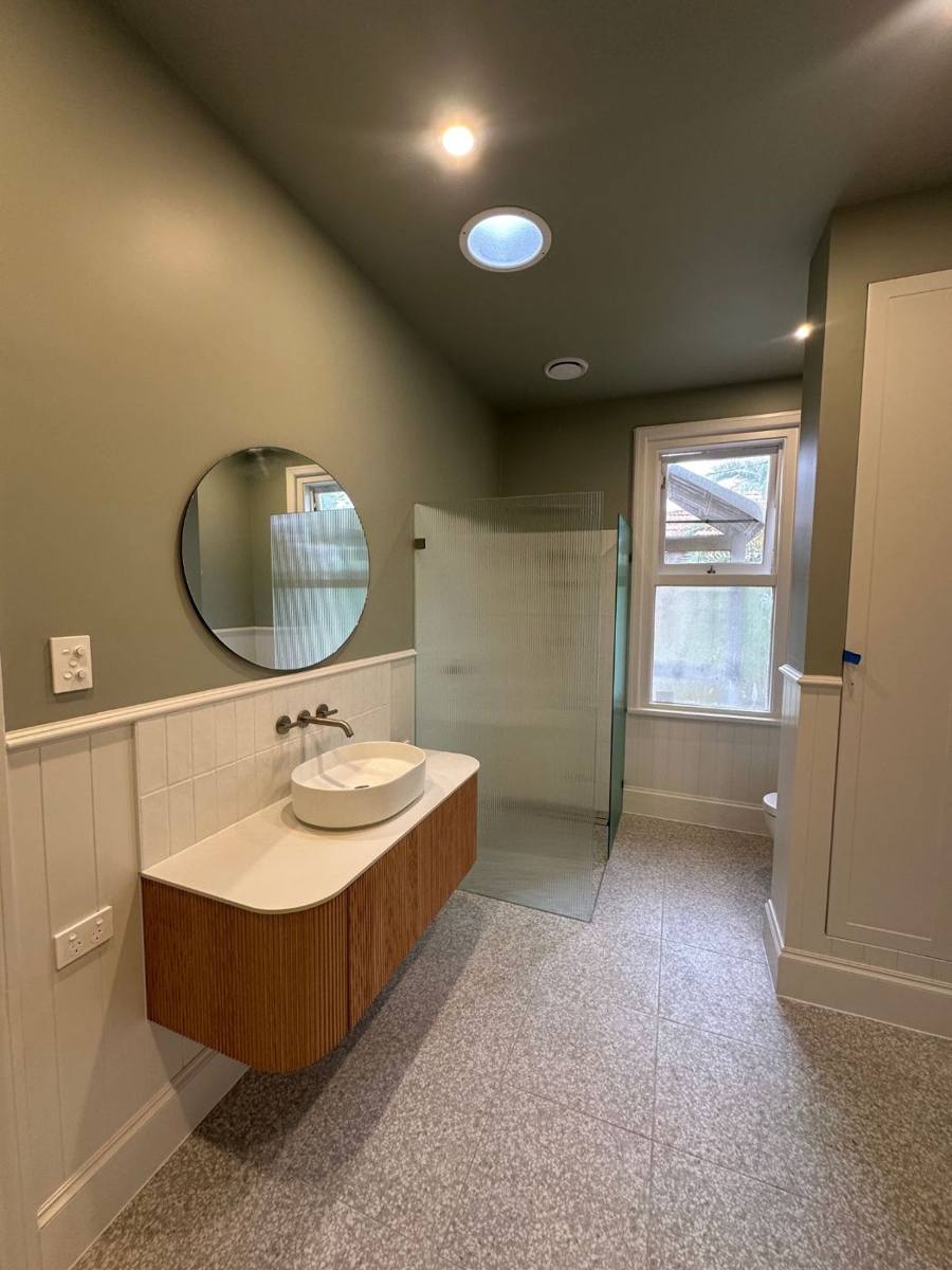 Finished bathroom with green walls, white panelling, timber wall-hung vanity and frameless shower
