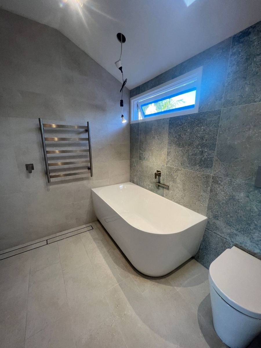 Freestanding bath against a stone-look feature wall with a strip drain in the floor