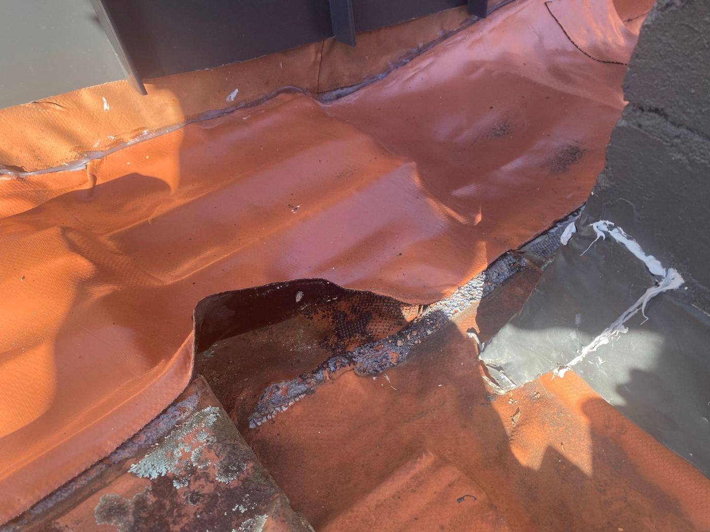 Split and patched lining in an old box gutter beside a wall