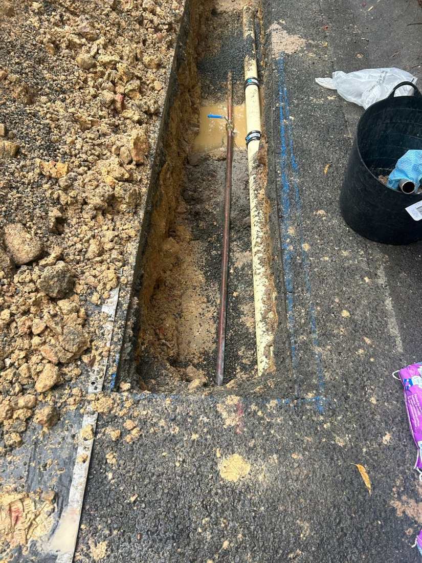 Narrow trench along a driveway with a new copper water line laid in it