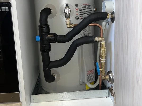 Storage hot water unit installed under a bench with lagged pipework and valves