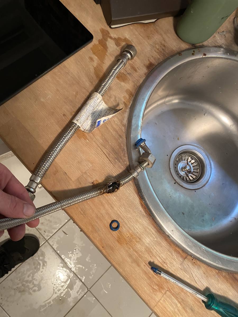 Burst braided flexible hose pulled out from under a kitchen sink, water on the floor