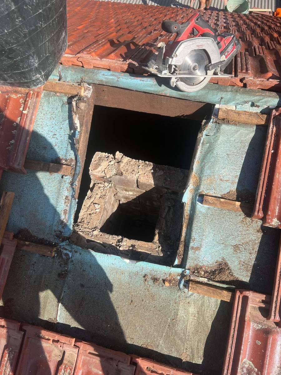 Old skylight removed from a tiled roof, showing the worn flashing and frame around the opening
