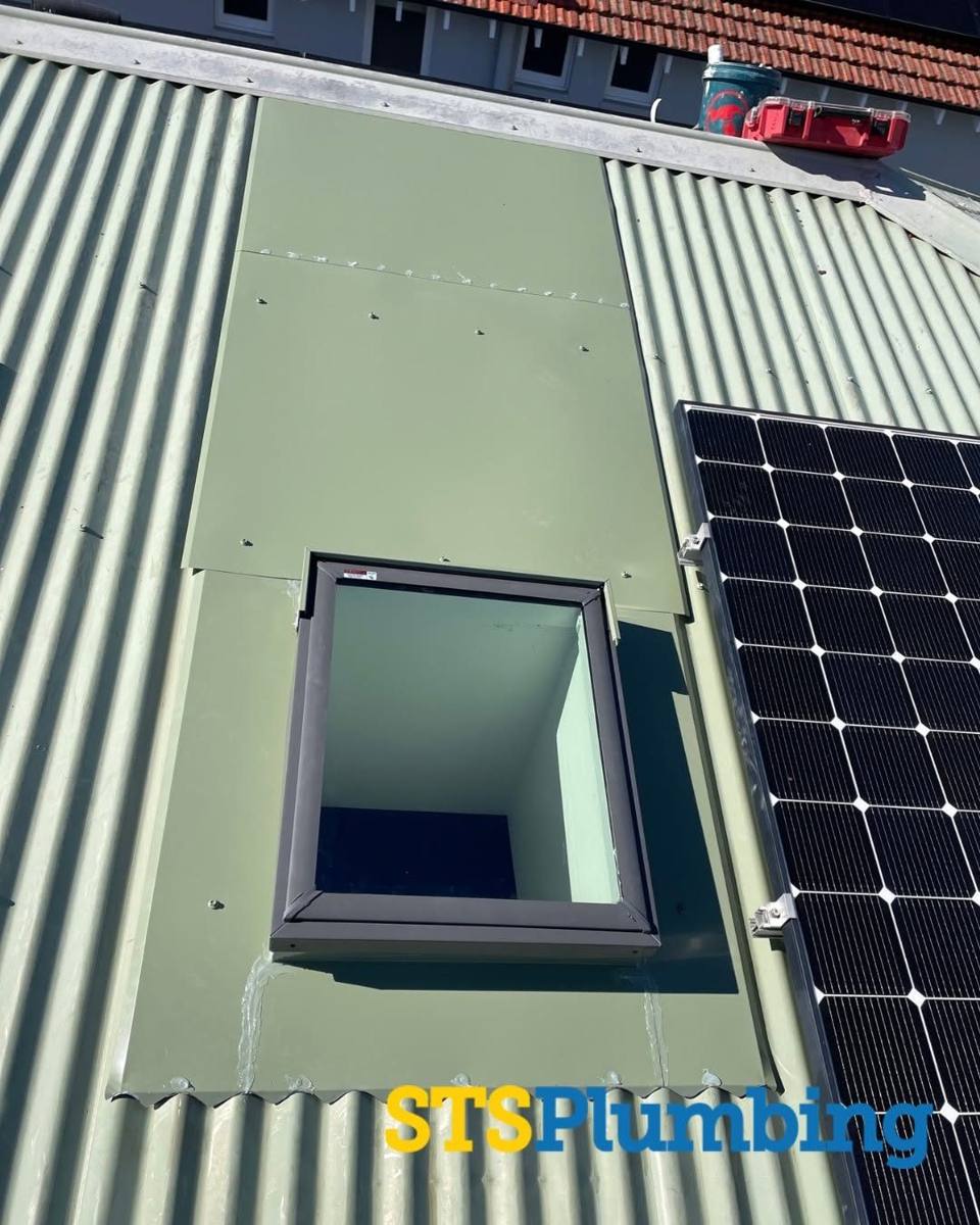 Skylight upstand being fitted through a metal roof beside solar panels