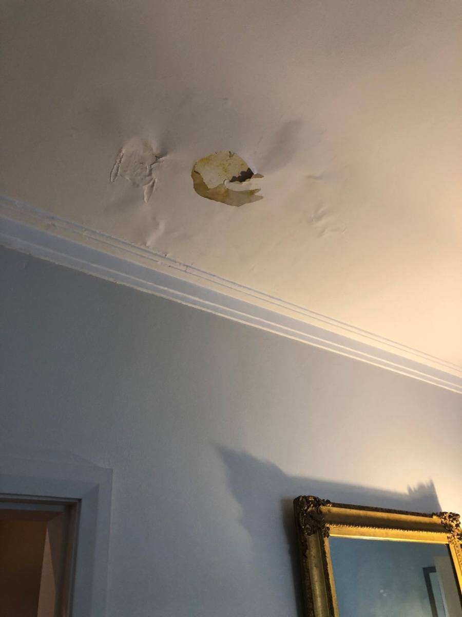 Water stain and bubbling paint on a ceiling below a bathroom in an apartment block