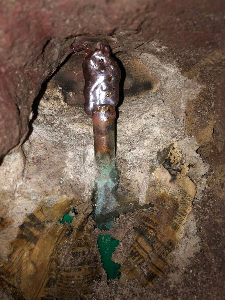 Corroded copper water pipe exposed inside an opened brick wall