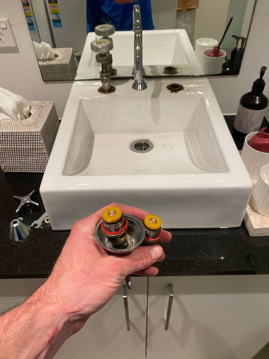 Plumber holding the old tap top out of a dripping basin tap
