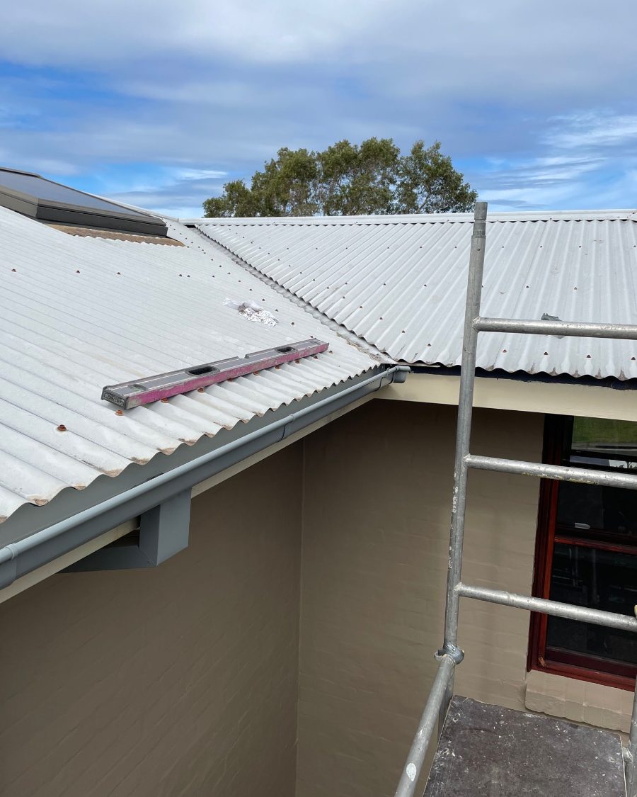 A new gutter along a metal roof edge, with the ladder used for access